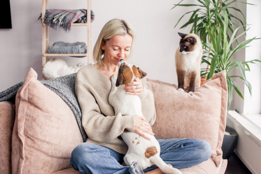 Glad medelålders kvinna kelar med sin hund och katt i en soffa