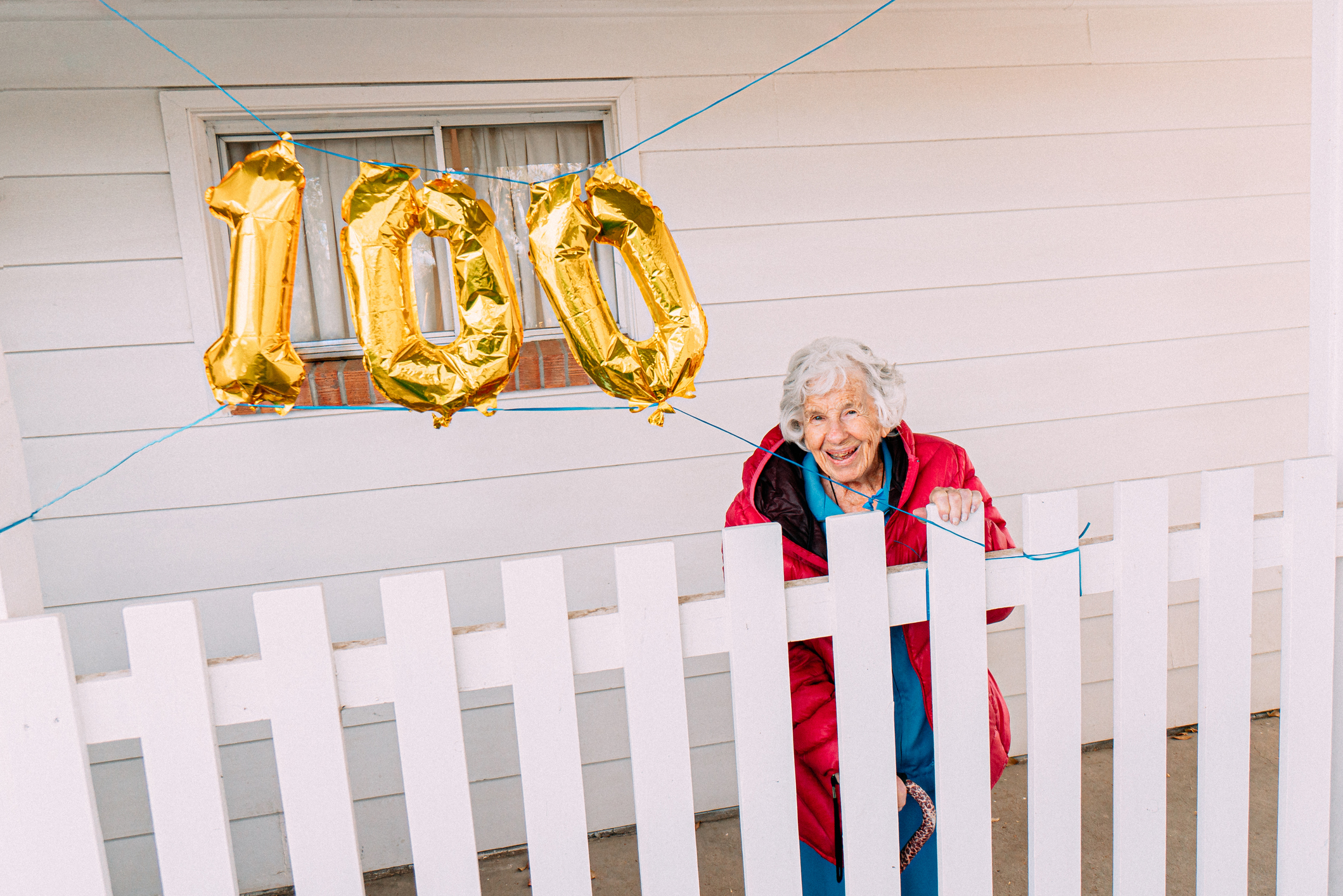 Äldre kvinna på veranda med guldballonger i siffran 100