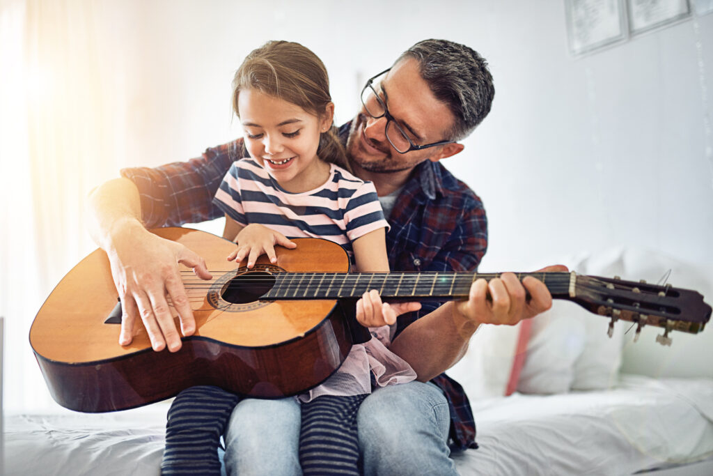Pappa med sin dotter i knät spelar gitarr