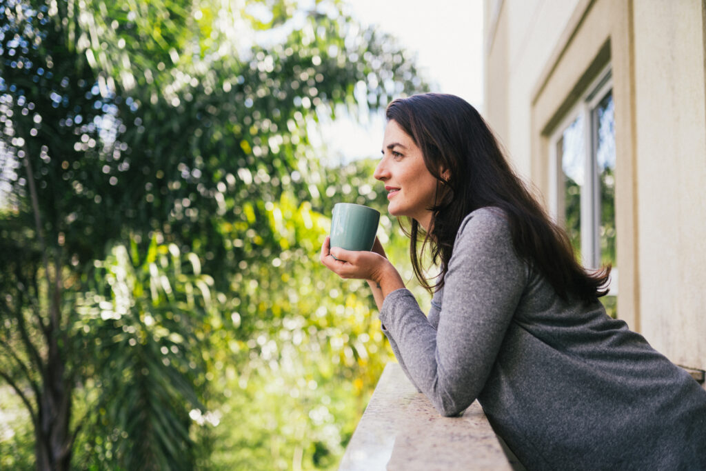 Kvinna njuter av skogsbad med en kopp kaffe på balkongen