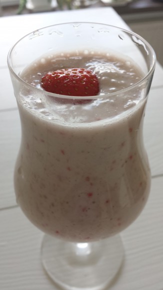 Smoothie i glas toppad med en jordgubbe på ett vitt träbord