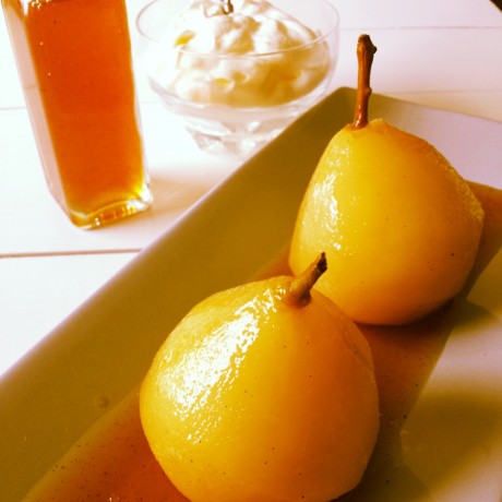 Två päron på ett fat. En flaska med sås och en skål med vispad grädde på ett vitt bord