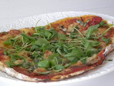 Pizza dekorerad med ruccolasallad på ett vitt fat