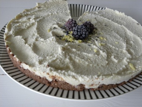 Raw cheesecake dekorerad med citronskal, lavendel och björnbär på ett vitsvartrandigt fat