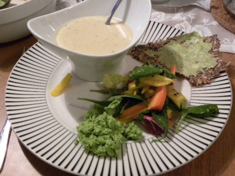 En flat tallrik med en vit soppskål med soppa, sallad, fröknäcke och ärthummus