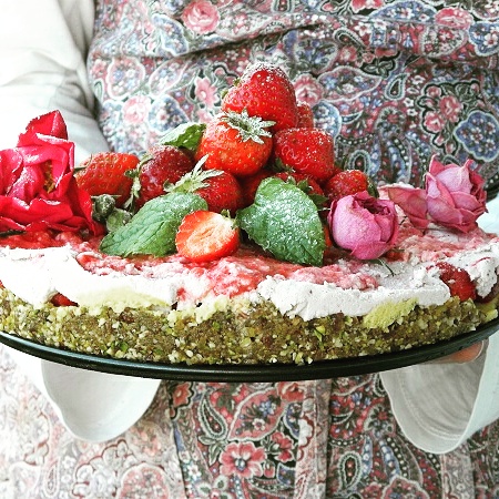 Någon klädd i förkläde håller en tårta dekorerad med jordgubbar och rosor